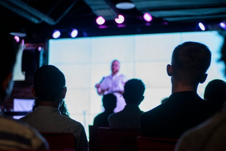 Audience in a dark room watching a speaker and a bright presentation screen